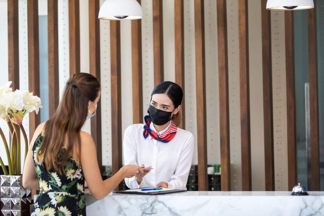 Receptionist attending a guest while following the covid protocol for hotels.