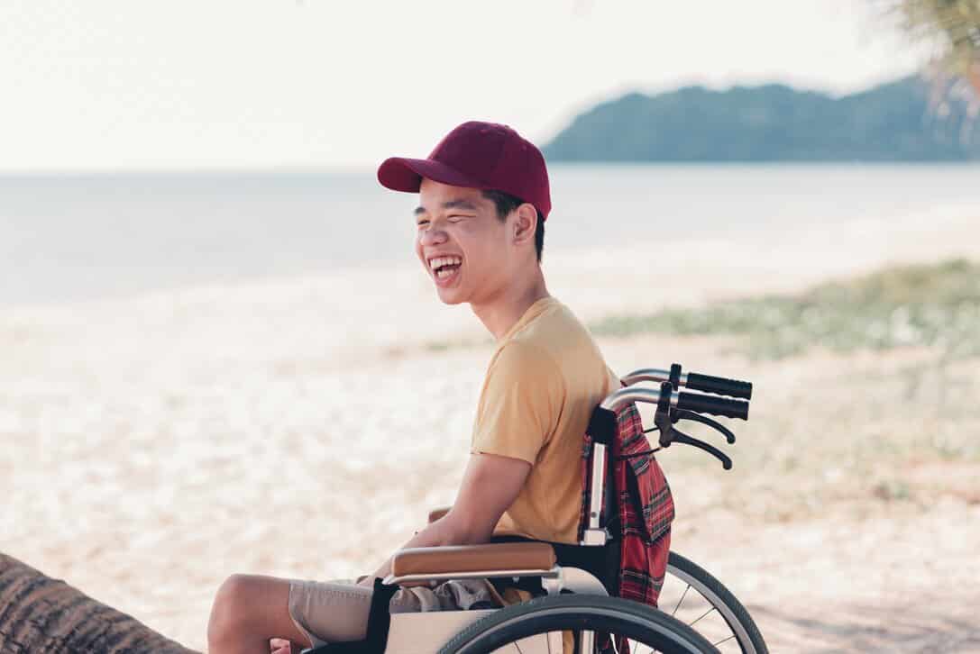 Teenager in a wheelchair laughing at the beach in Playa del Carmen, Mexico, which is one of the best vacation spots for disabled people.