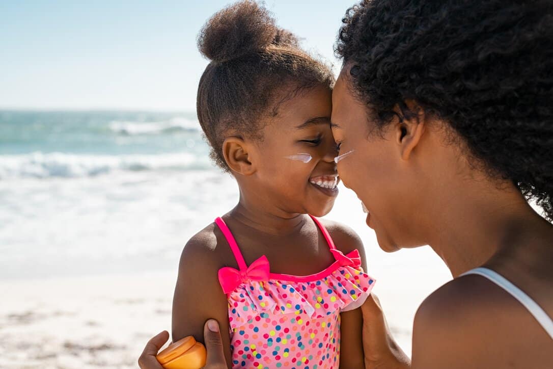 Woman putting on sunscreen with her daughter smiling