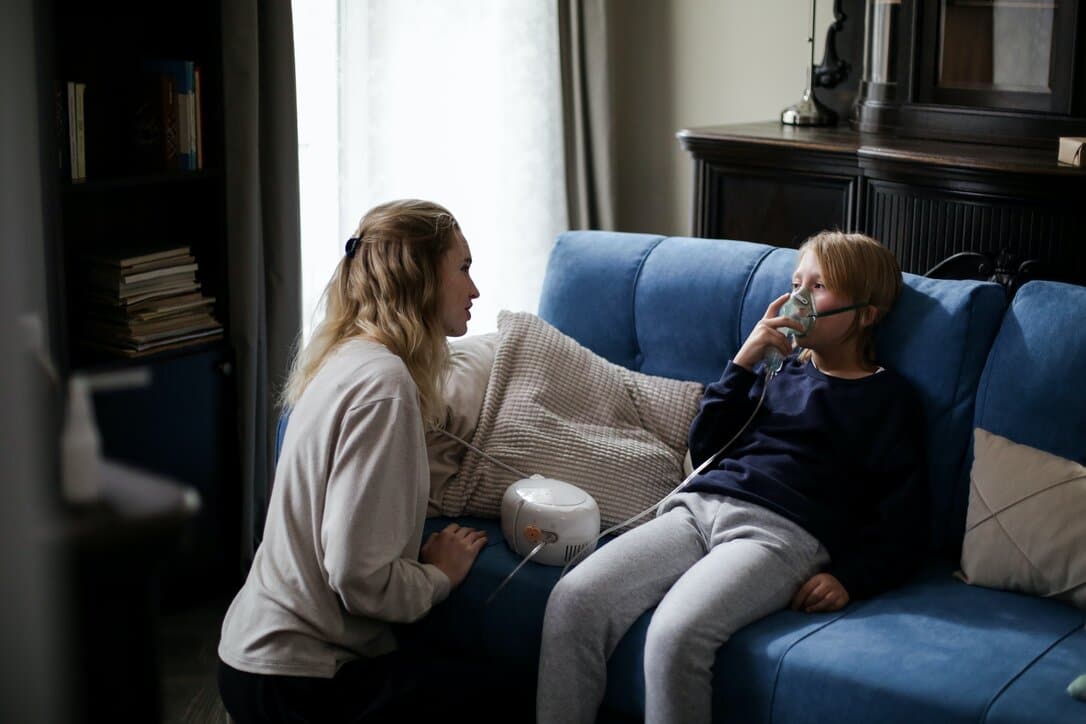 Child doing nebulizations to help his asthma episode, being helped by his mom.