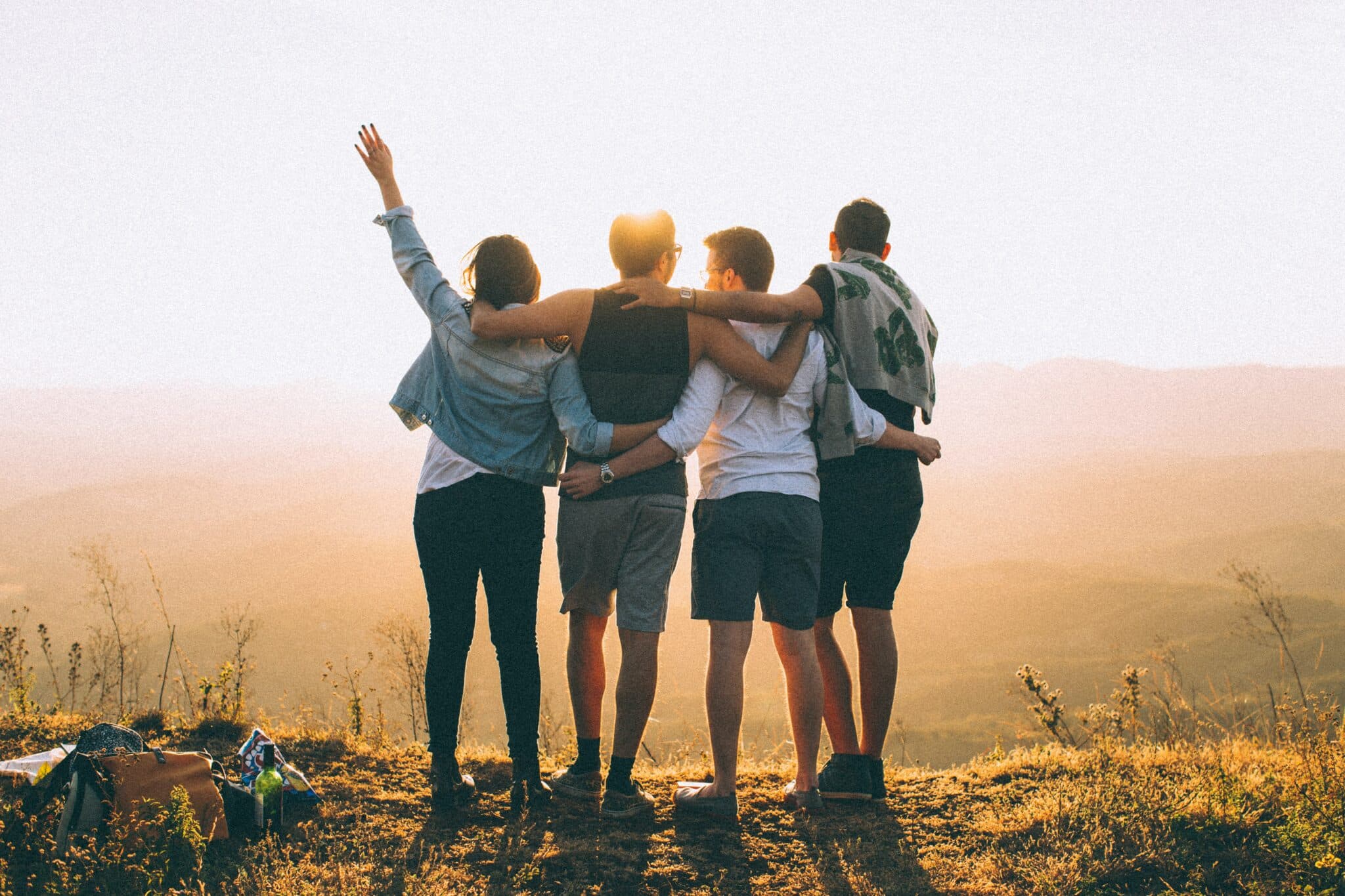 A group of four friends hugging while facing a mountains landscape in joy, probably celebrating the end of the pandemic.