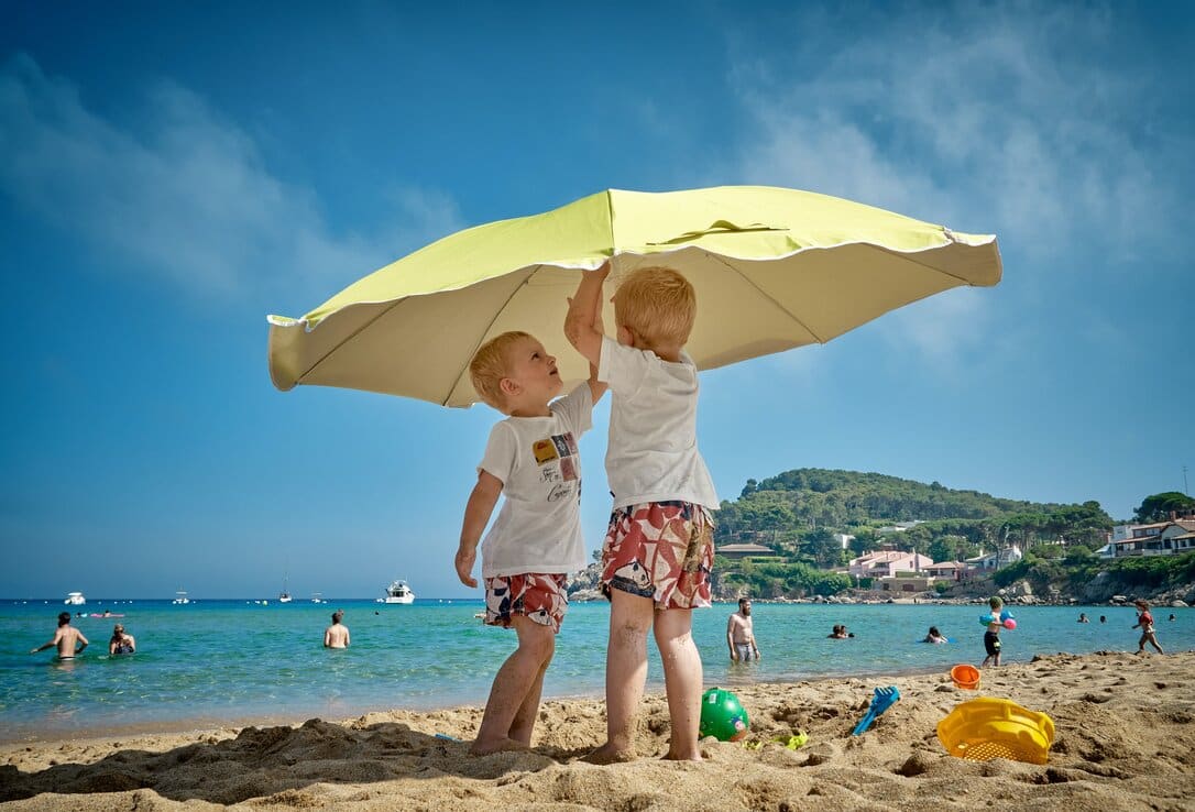 Two kids protecting themselves from the sun with a parasol at the beach